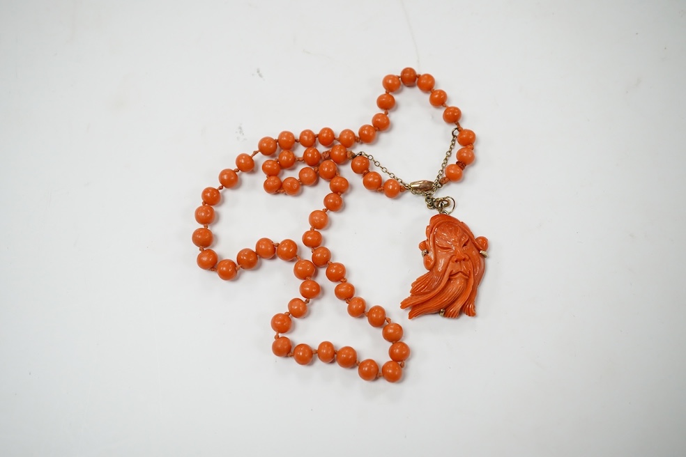 A single strand coral bead necklace, with a coral pendant carved as the face of a gentleman, overall 48cm. Condition - fair